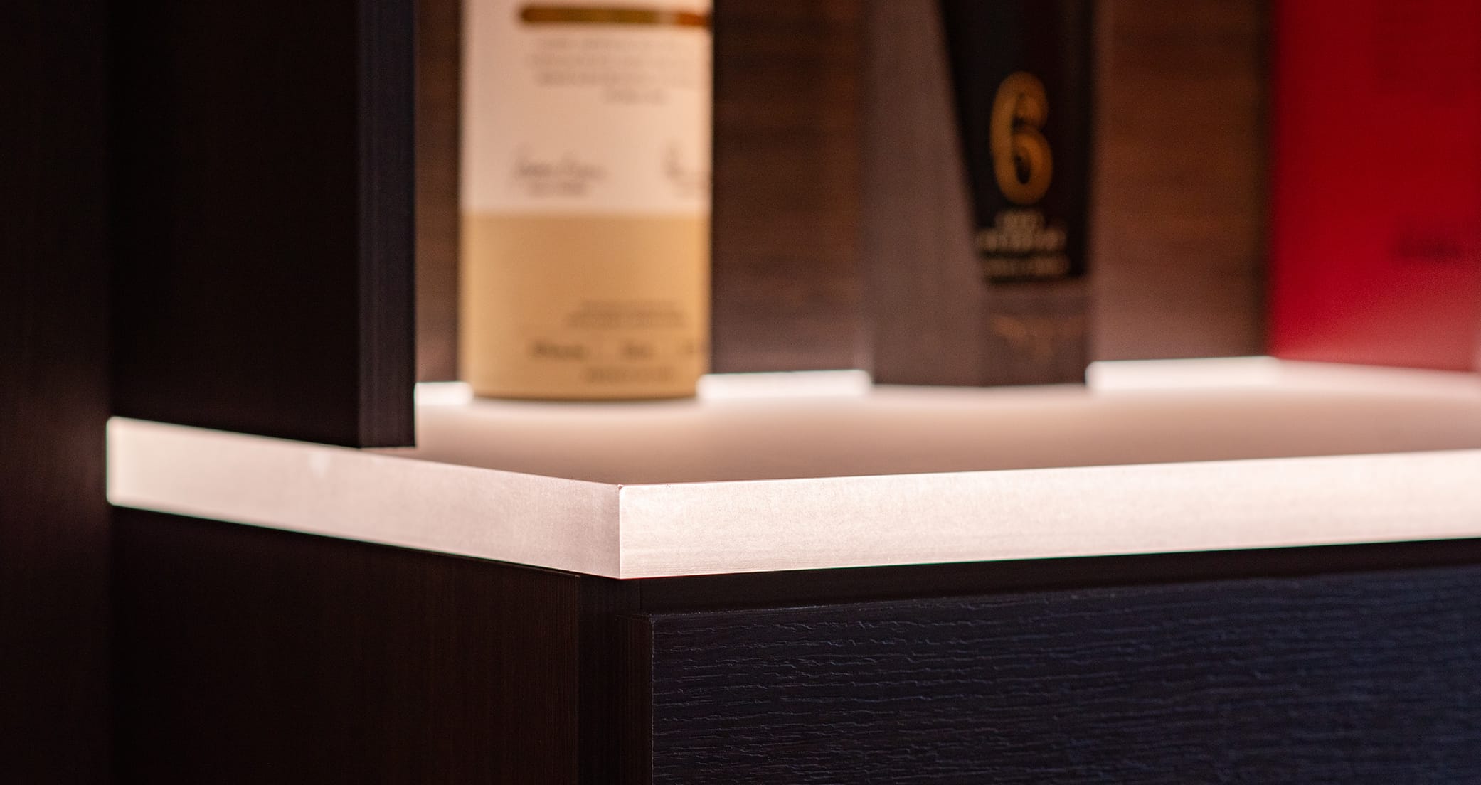 Close up detail of home wine bar storage with lit shelving and dark wood finish by California Closets
