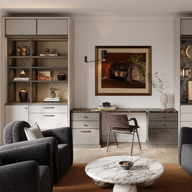 A modern home office featuring built-in shelves flanking a marble-topped desk, decorated with books, vases, and sculptures. The space includes a brown leather chair, two dark grey armchairs, and a round marble coffee table with a small bowl.