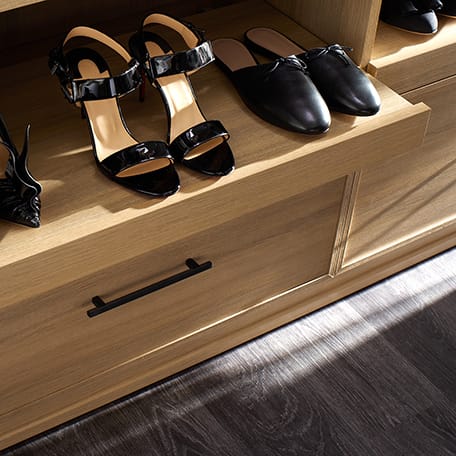 Custom walk in closet with pull out shoe shelf storage in light wood finish by California Closets